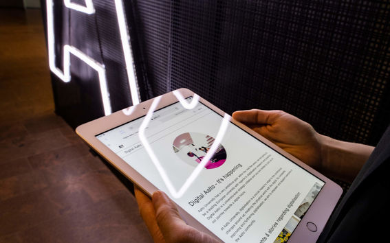 Up-close photo of hands holding an iPad, with the Aalto logo on the wall in the background.