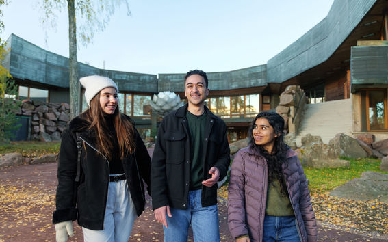 Three students, Amr in the middle, walking on campus with autumn leaves on the ground.