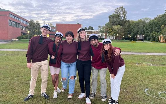 A group of students on campus wearing teekkari caps and matching colleges.