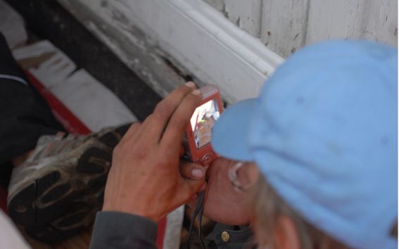 A person in a light blue cap taking a picture with a red digital camera