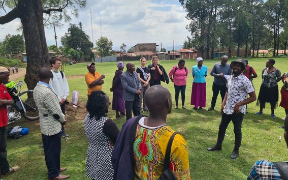 A group of people from Kenya and Finland standing on a grass field in Kenya and interacting in a circle