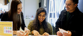 Three students, Anubhuti in the middle, at a career fair smiling and looking at brochures.