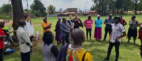 A group of people from Kenya and Finland standing on a grass field in Kenya and interacting in a circle
