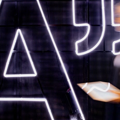 Person holding tablet walking by lighted Aalto logo A 