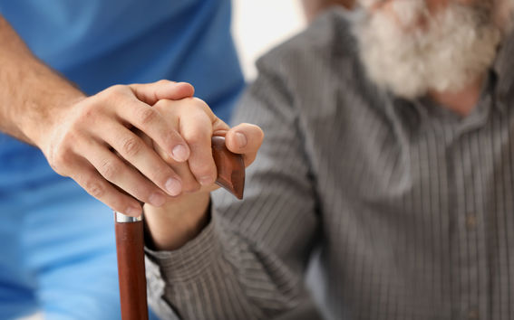 Senior man and young caregiver holding hands on walking stick, closeup