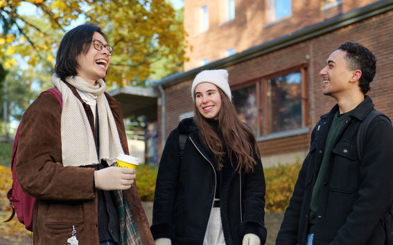 Three students, Olia in the middle, chatting and laughing in front of a student housing building.