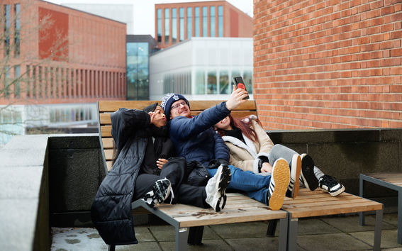 Three students taking a selfie donned in winter clothes on campus, Owein in the middle holding the phone.