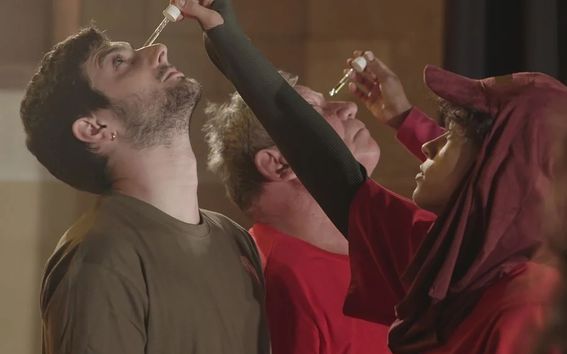 Still image from performance, where a person is dropping liquid into someone's eye.